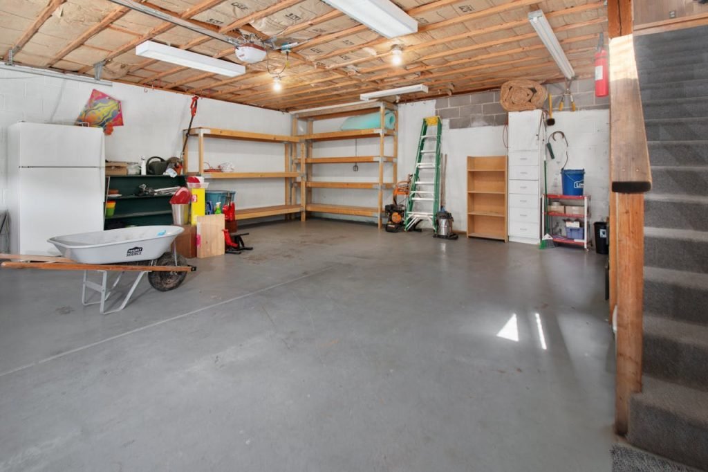 garage-hall-in-house-17181949 Spacious garage interior with storage shelves, tools, and a wheelbarrow, ideal for home organization.